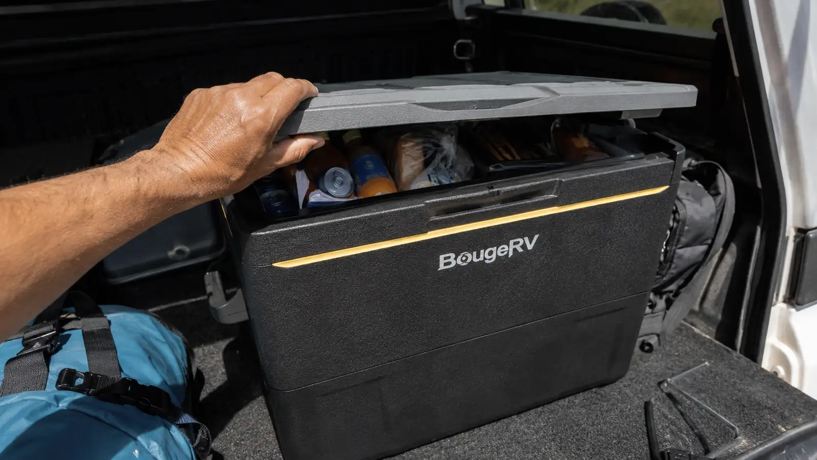 Hand lifting the lid of the BougeRV 12V fridge to show cold drinks and packed groceries inside