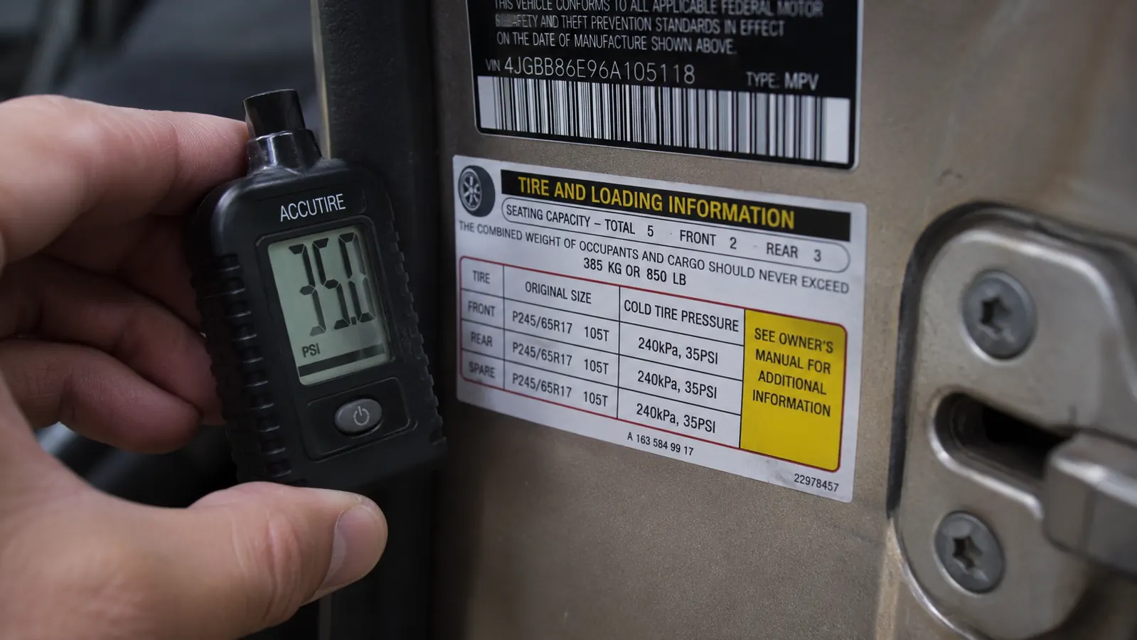 A tire inflator's digital gauge shown up close reading a specific PSI number, positioned near a door-jamb tire pressure sticker
