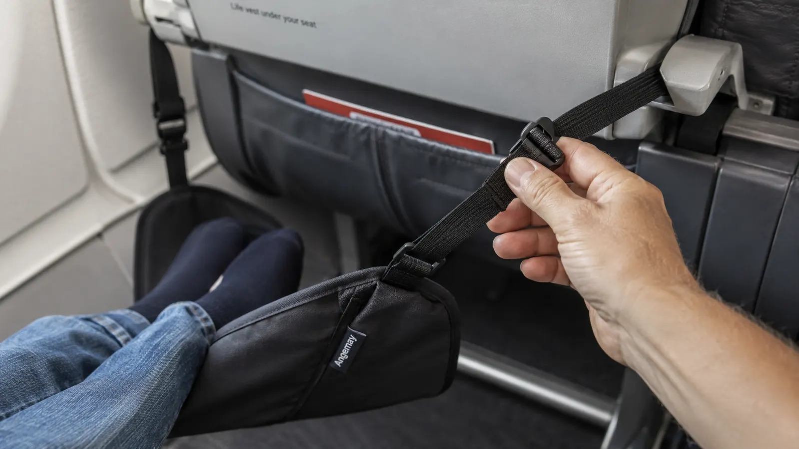 Hand adjusting the strap of a footrest hammock attached to an airplane tray table arm