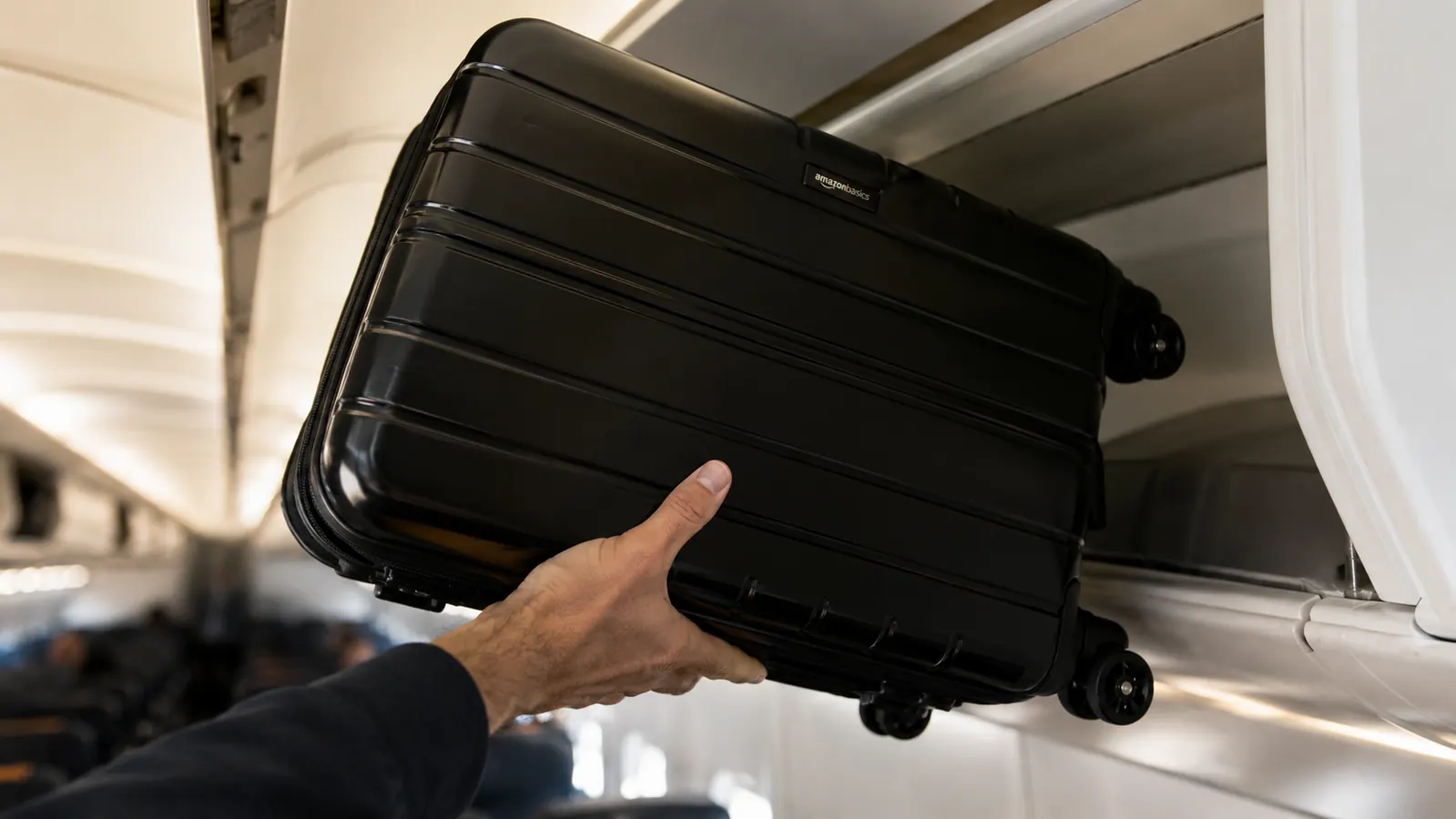 Hand lifting a black hardside carry-on into an overhead airplane bin