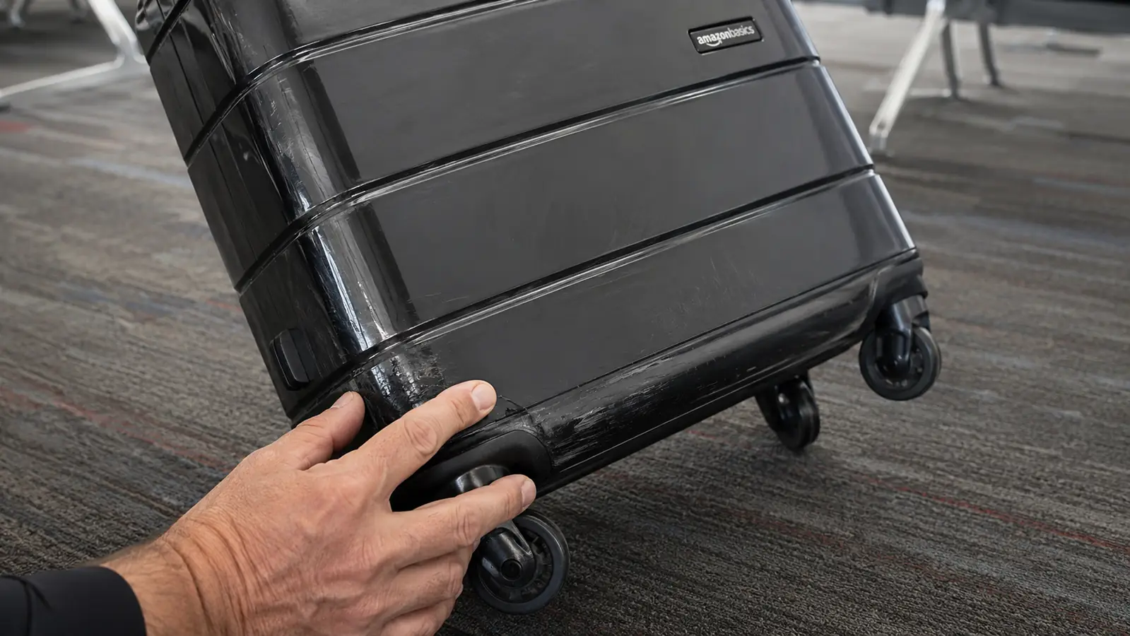 Close-up of a hand tilting the carry-on to inspect a scuffed corner and a rear spinner wheel