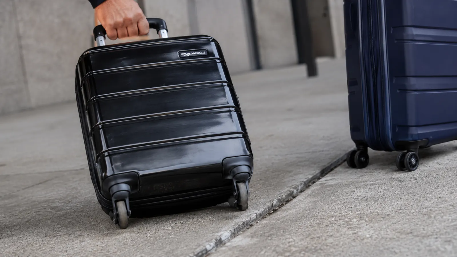 Close-up of the Amazon Basics carry-on's spinner wheel and telescoping handle next to a smoother, sealed-bearing Samsonite wheel