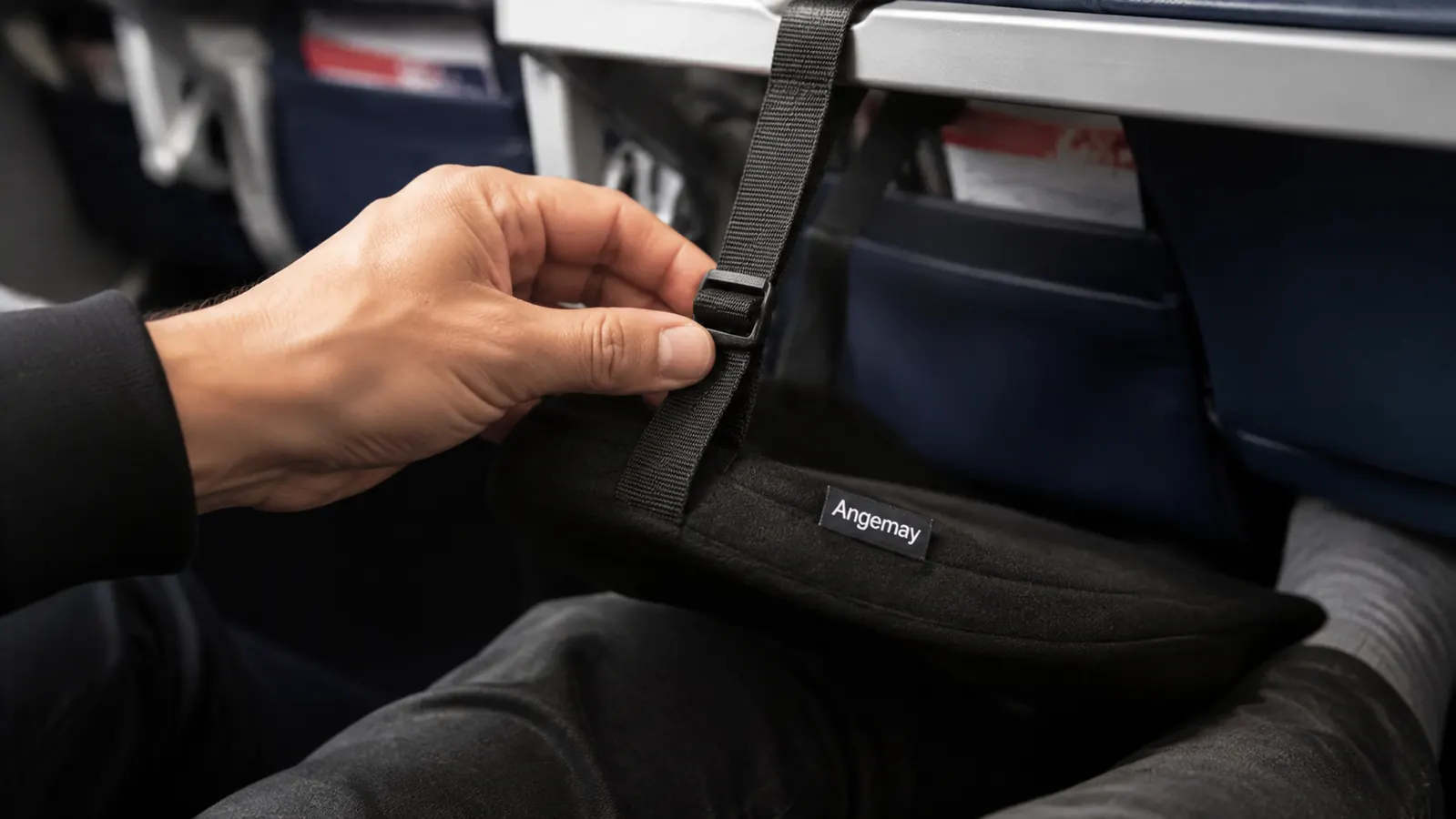 Hand adjusting the strap and buckle of the Angemay footrest hooked over an airplane tray table arm