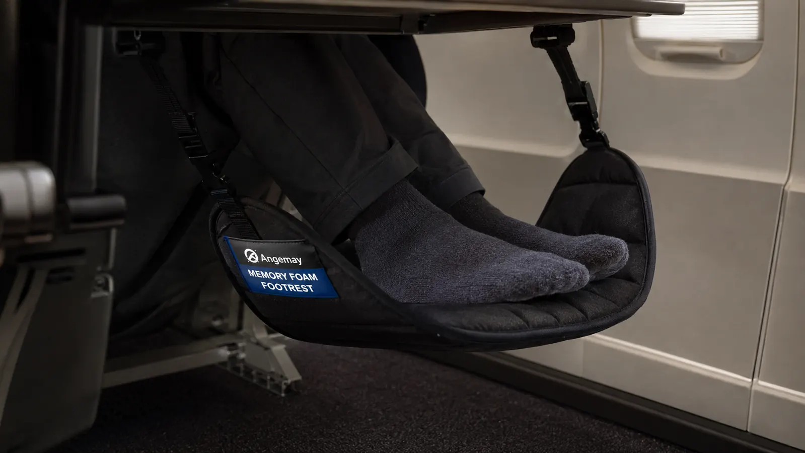 Close-up of a traveler's feet resting in the memory foam top of the Angemay footrest under an airplane seat