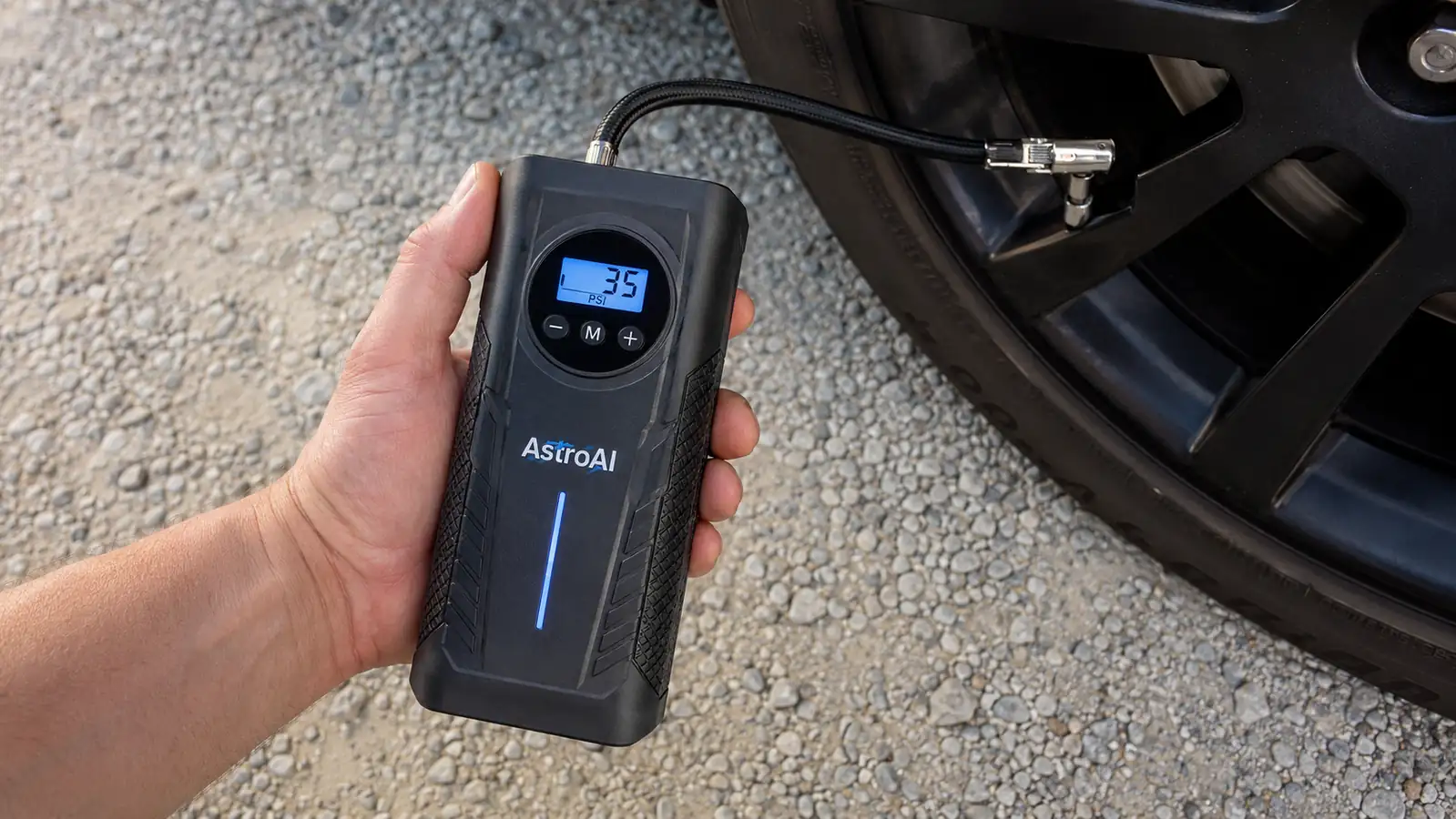 Close-up of a hand holding the AstroAI inflator's digital display reading 35 PSI while attached to a tire valve stem