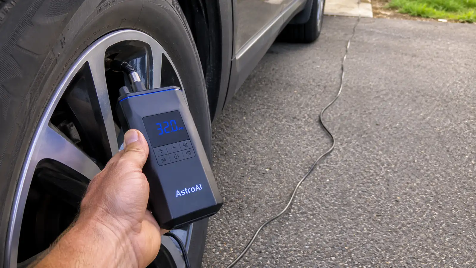 Hand holding the AstroAI inflator's digital display up close while the compressor runs against a rear tire valve stem