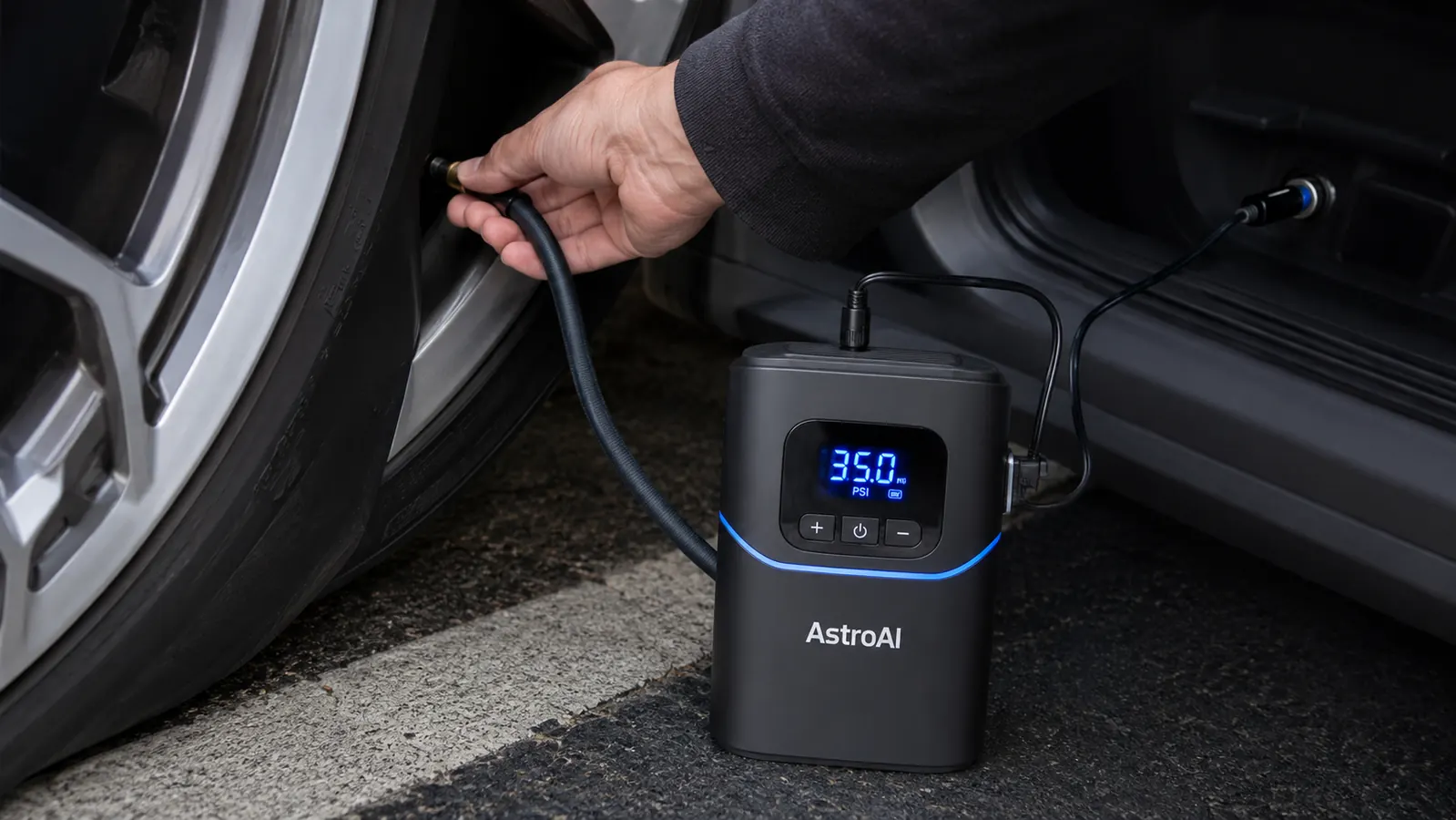 Hand holding the AstroAI portable tire inflator against a car tire valve stem with the digital gauge lit up