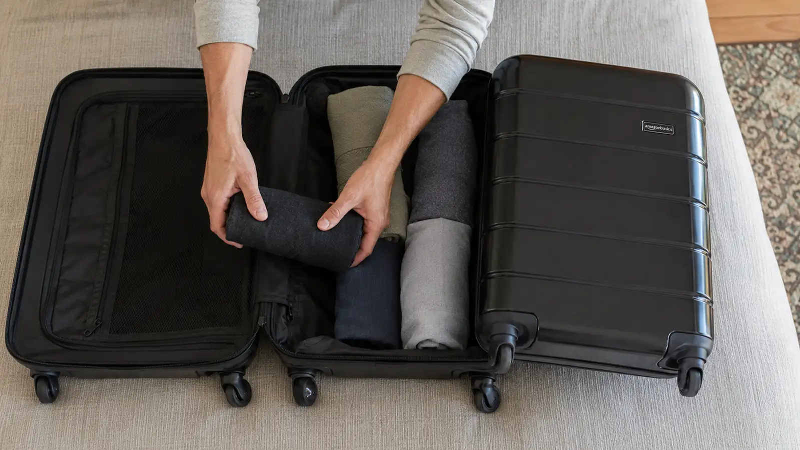 Hands rolling folded clothing into tight bundles inside an open hardside carry-on